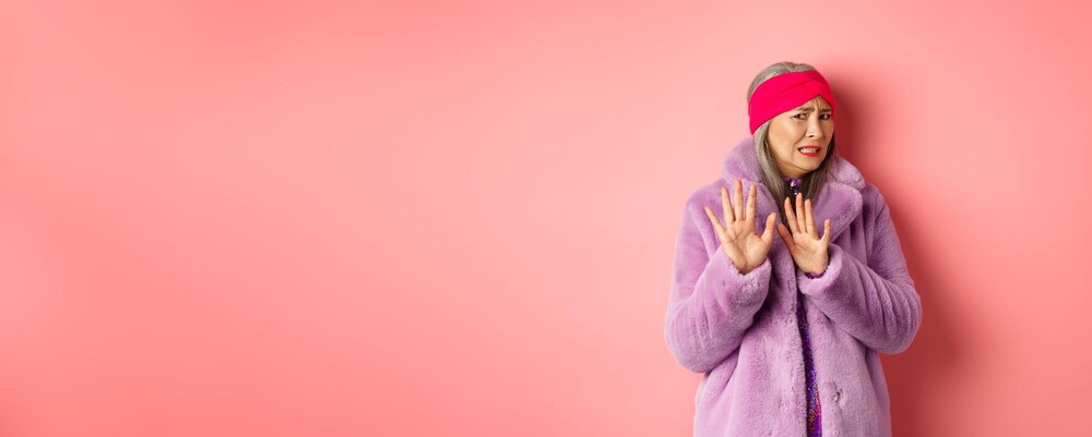 Portrait of stylish asian senior woman in purple winter coat cringe from something disgusting frowni